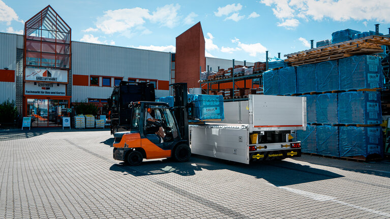 Mit einem Stapler werden vor einem Baumarkt Säcke mit Baumaterial in einen Anhänger verladen. | © Humbaur GmbH